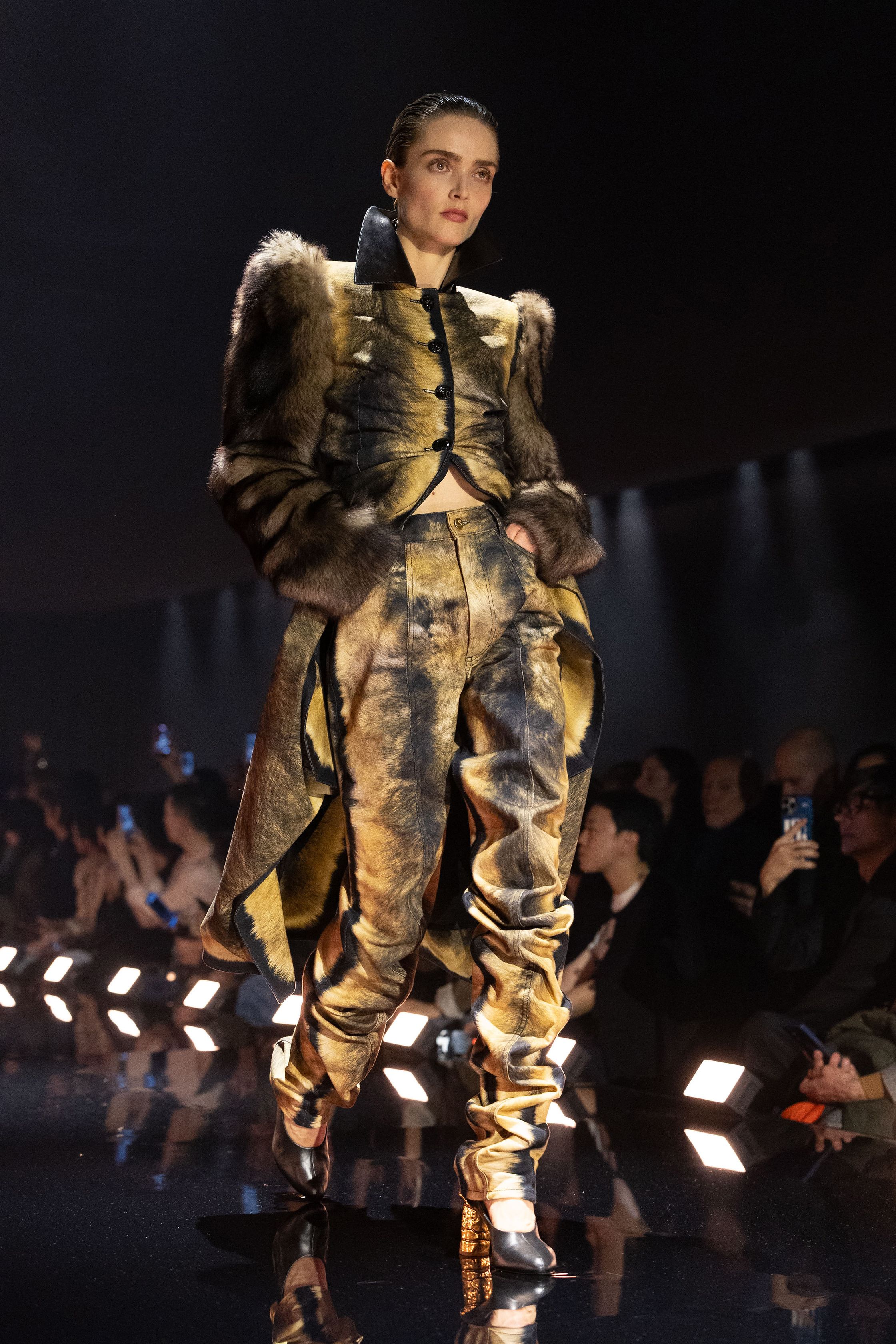 Schiaparelli 2026秋冬系列延续品牌标志性的超现实主义美学，在金色灯光的T台上呈现极具雕塑感的廓形。沙金色与黑金色成为主调，褶皱礼服、雕塑式西装与高腰裙装强化身体线条。经典的金属装饰、夸张肩线以及精致刺绣细节构成强烈视觉符号，使整场秀既华丽又充满戏剧张力。设计师通过结构与面料的张力对比，让高级定制的艺术精神融入现代女性衣橱-顽石频道趋势研究